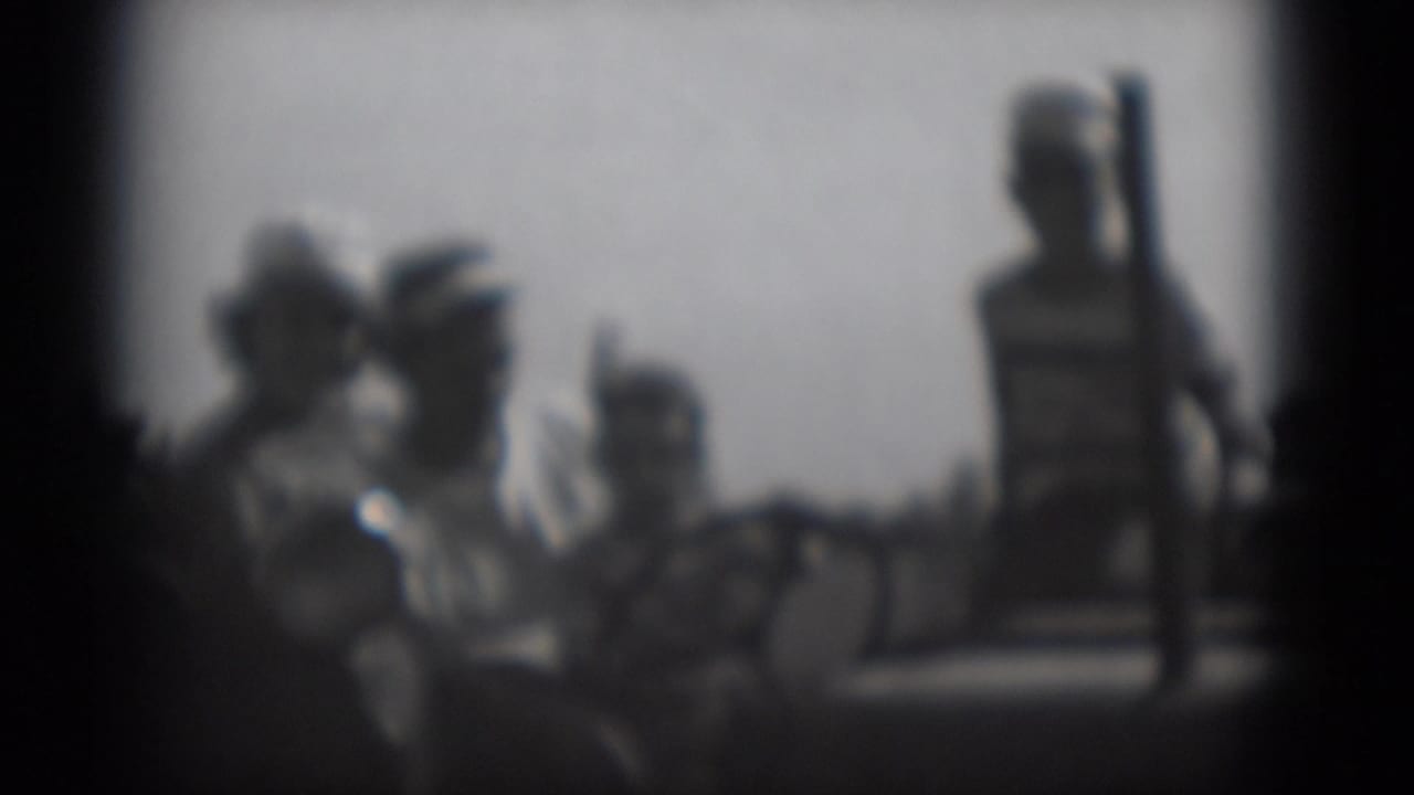 Blurred group of people outdoors, with one standing figure near the right edge.