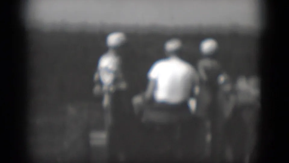 Middletown, Pennsylvania 1975 home-movie frame showing people near parked farm equipment beside a light-sided building.