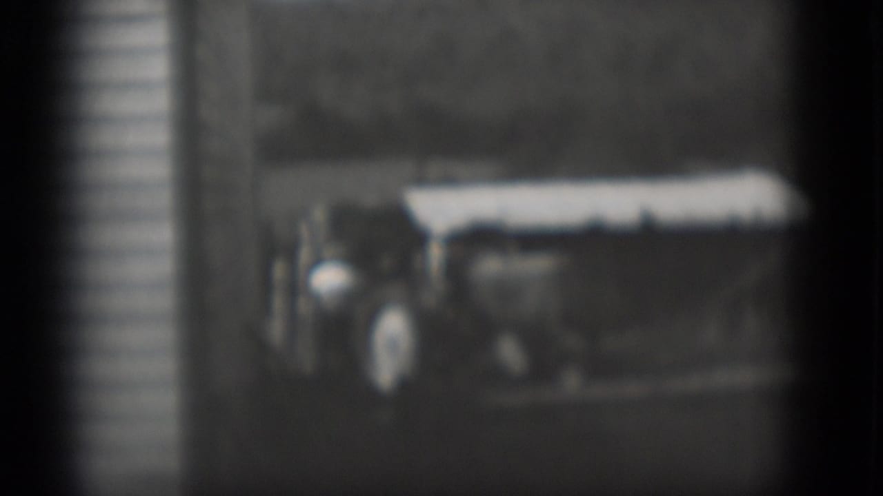 Soft 1975 Middletown frame of a tractor-like farm vehicle parked near a white building, with people partly visible at the side.