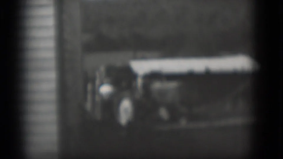 Soft 1975 Middletown frame of a tractor-like farm vehicle parked near a white building, with people partly visible at the side.