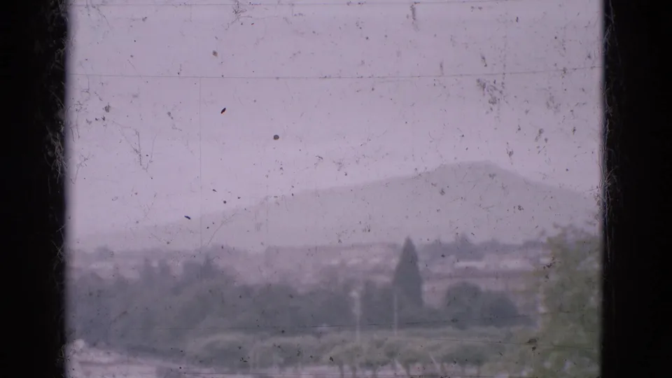 1975 Portugal travel footage frame showing a hazy mountain landscape with trees and distant settlement through scratched 8mm film.