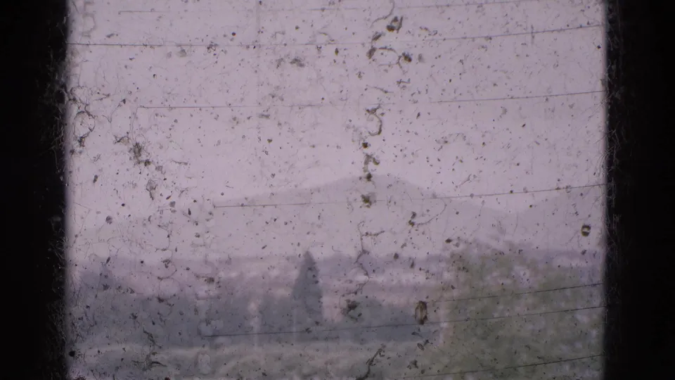 1975 Portugal 8mm frame looking through dirty window glass toward soft mountain ridges and treetops.