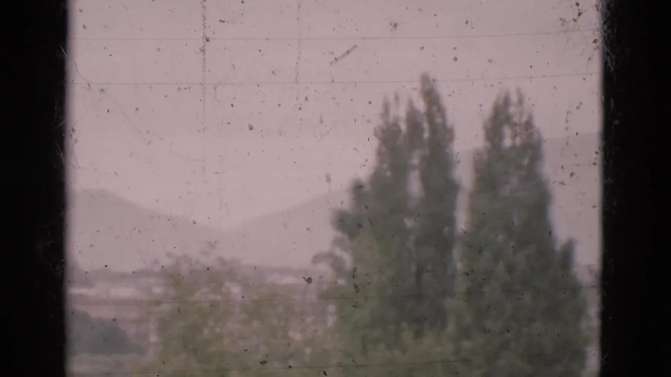 A final 1975 Portugal frame shows blurred treetops and hazy hills through scratched, dusty window glass.