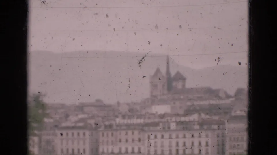 Soft 8mm frame of a Portuguese townscape with dense rooftops, a church-like structure, hills, and visible film dust.