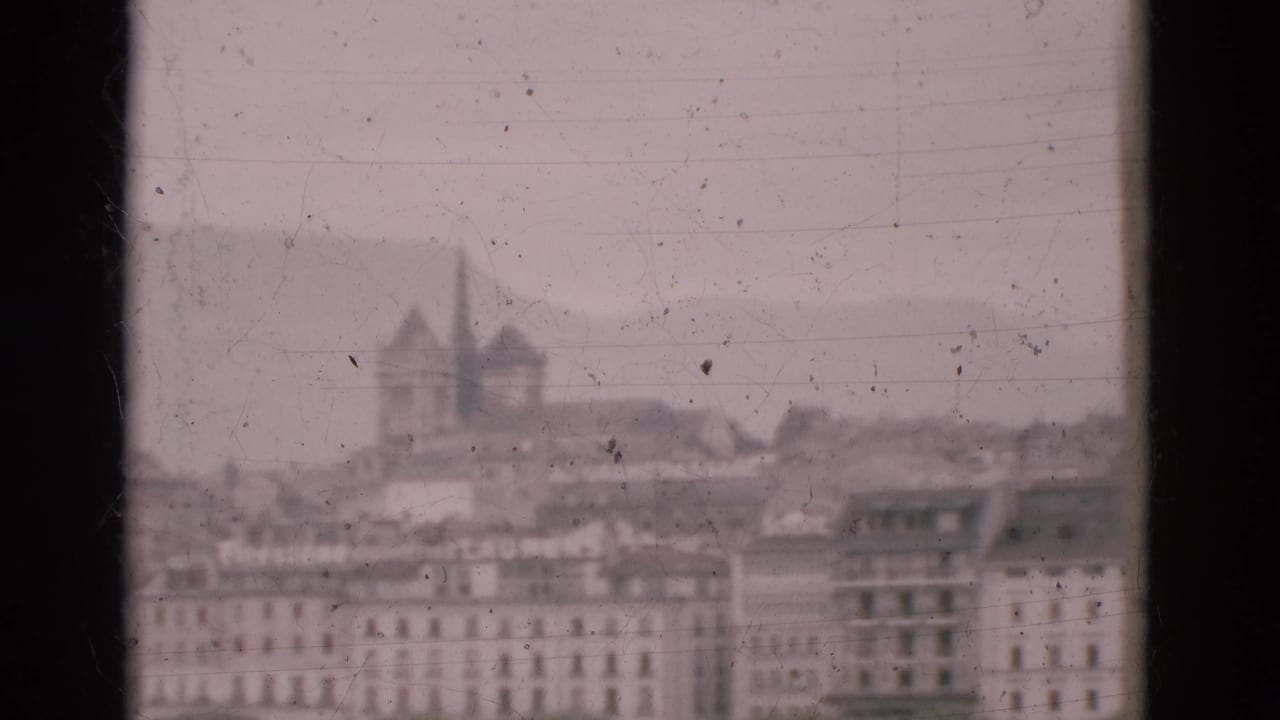 Soft city skyline behind a dark window mullion, with twin spires above rooftops.