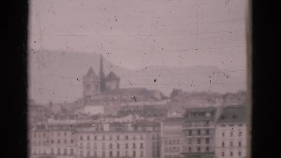 1975 Portugal travel footage frame with a hazy cityscape, distant twin-spired building, and dark window divider in the foreground.