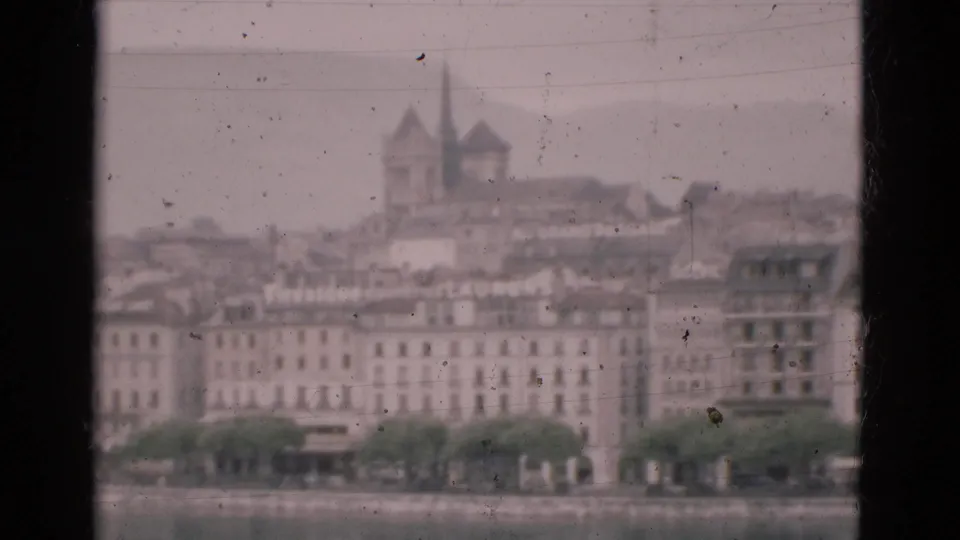 Final 1975 Portugal frame showing a muted waterfront city view through a window, with rooftops and twin spires in soft focus.