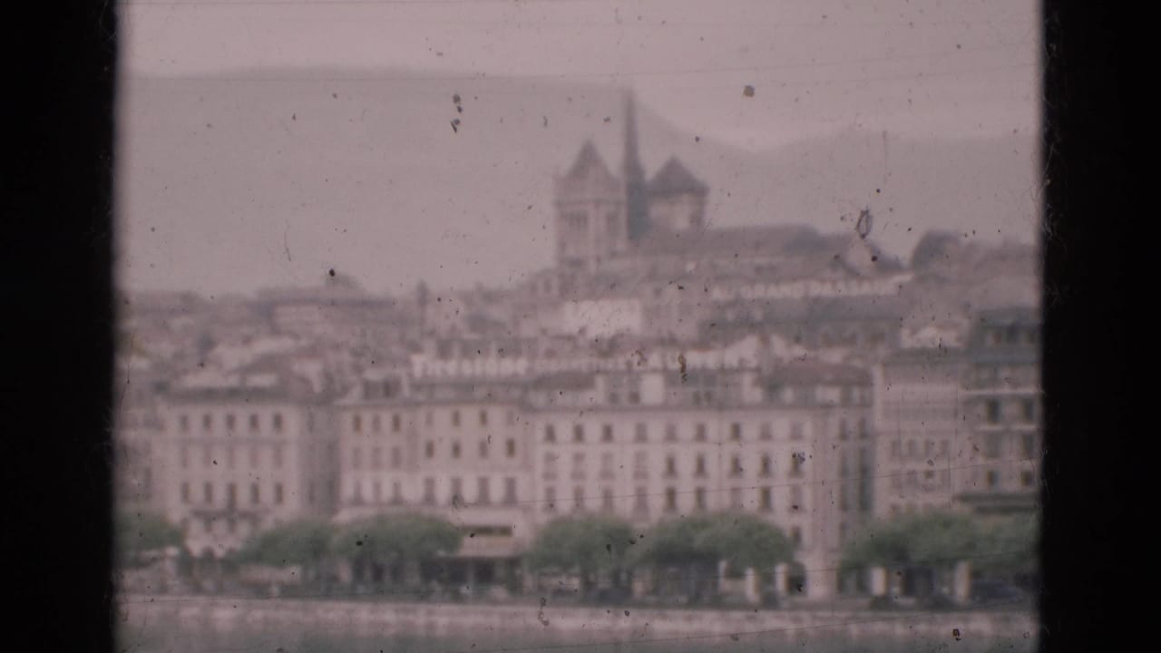 Window-framed hazy waterfront city view with pale buildings and a distant tower.