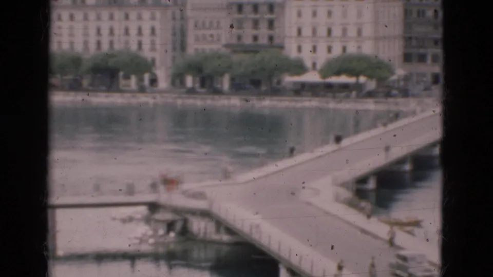 1975 8mm view of a Portugal waterfront with pale buildings, trees, river water, and a bridge or pier in the foreground.
