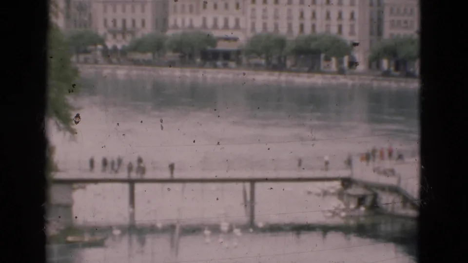 A 1975 Portugal waterfront view shows a bridge and small distant groups on the promenade, framed by dark window mullions and soft 8mm grain.