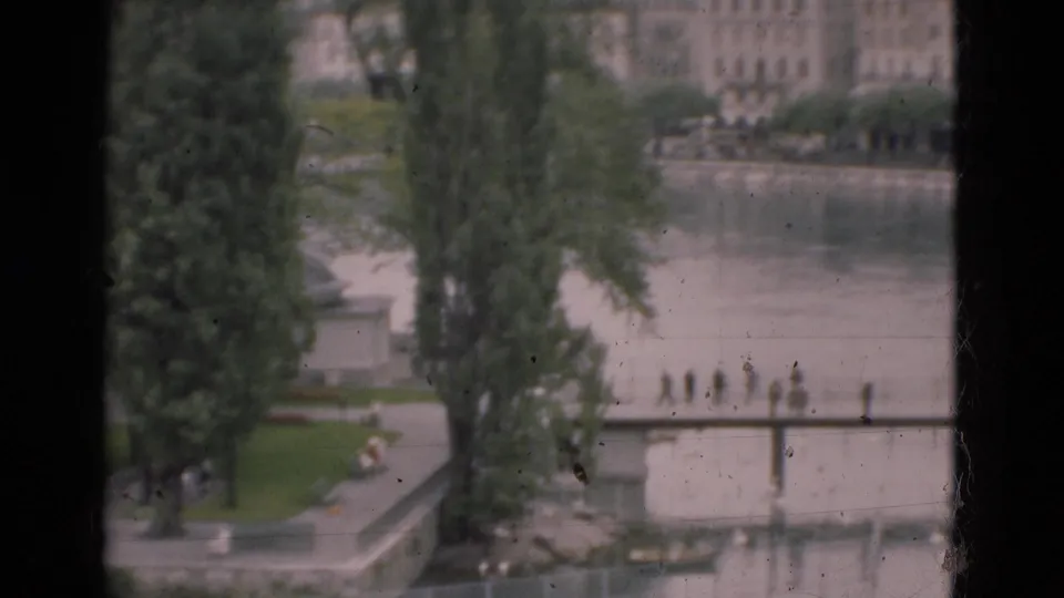 The final 1975 Portugal frame reveals more park greenery and tall trees beside the riverside promenade, with distant pedestrians and buildings beyond.