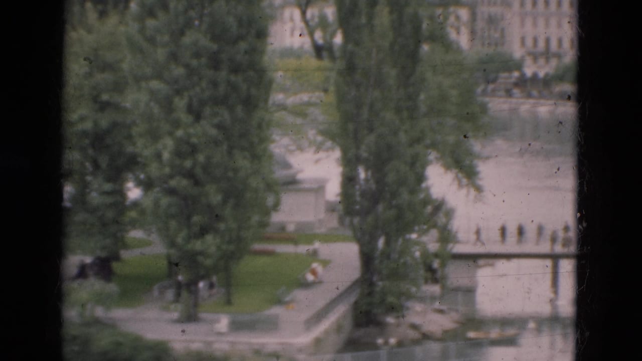 1975 Portugal home-movie view of a riverside park, bridge, trees, and distant buildings seen from an elevated window or overlook.