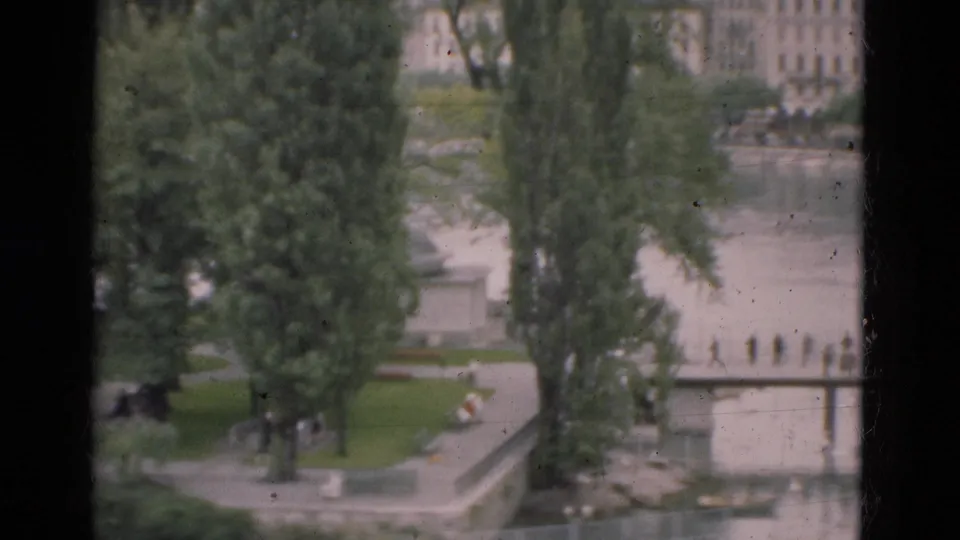 1975 Portugal home-movie view of a riverside park, bridge, trees, and distant buildings seen from an elevated window or overlook.