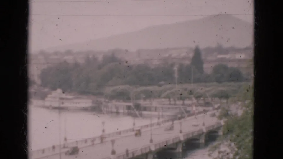 A faded 1975 Portugal travel frame shows bridge traffic over a river, with trees and hazy hills beyond the crossing.