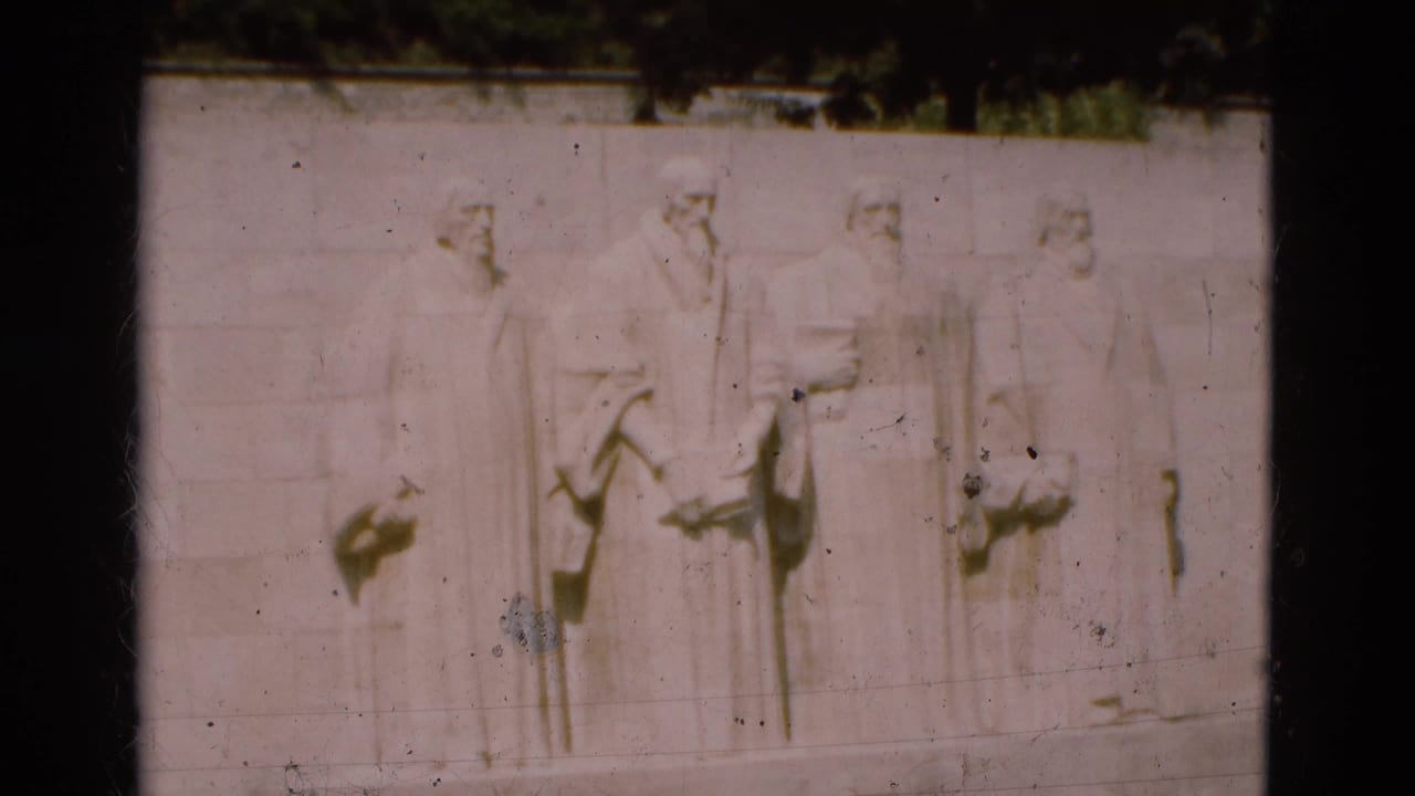 1975 Portugal 8mm frame showing four solemn robed male figures carved in relief on a pale outdoor stone wall.