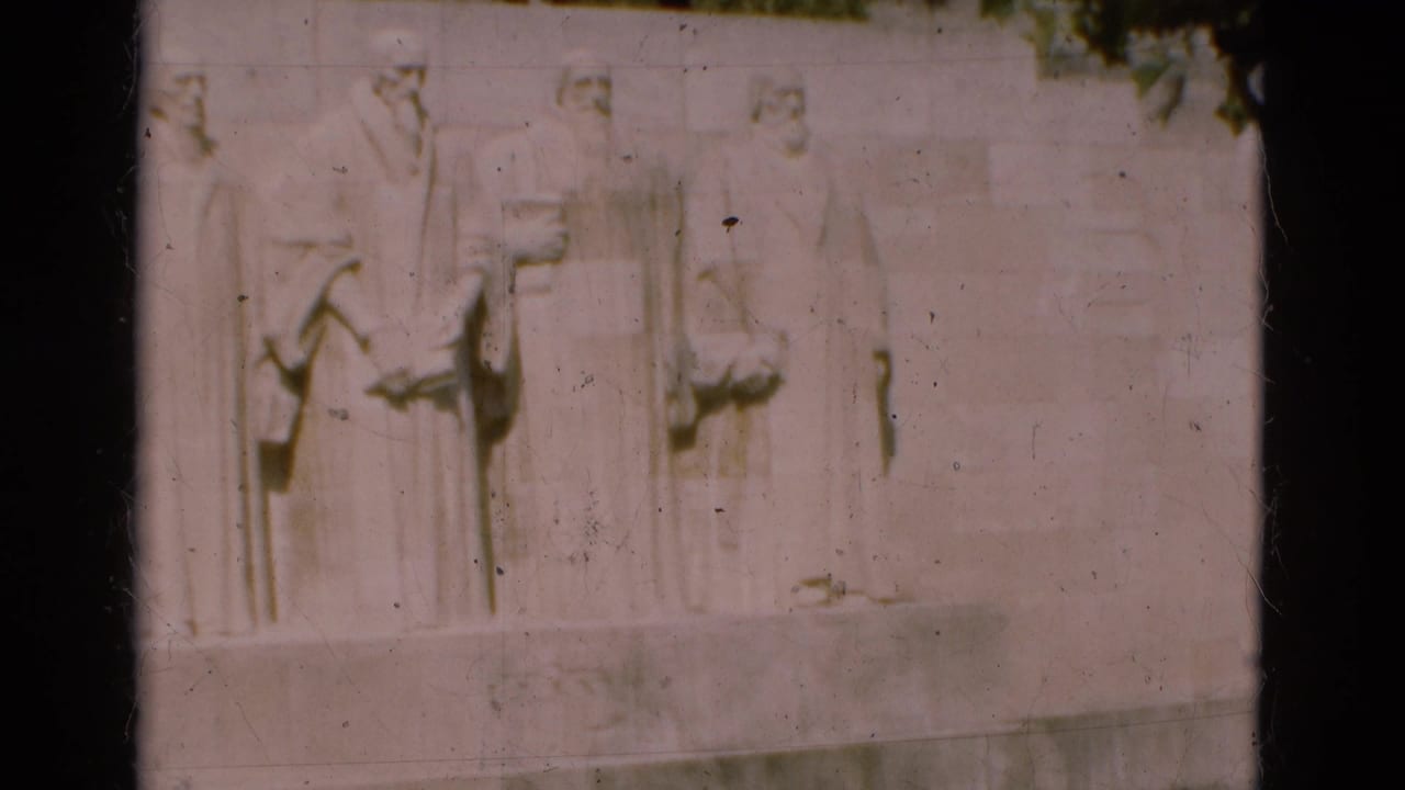 1975 Portugal home-movie frame showing pale sculpted bas-relief figures on a large stone monument wall.