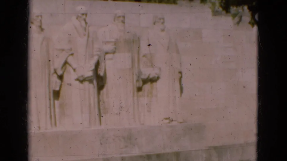 1975 Portugal home-movie frame showing pale sculpted bas-relief figures on a large stone monument wall.