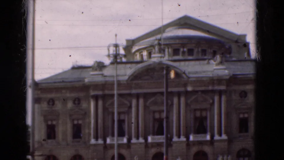 1975 Portugal frame showing a formal civic building facade with columns, arched windows, and dark film borders.