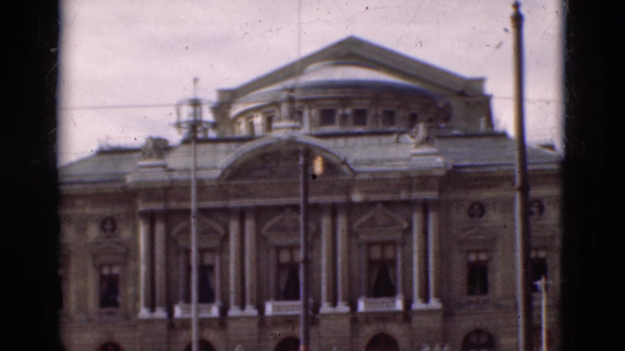 1975 Portugal 8mm frame showing a grand classical facade with columns, arched windows, roof detail, and street lamps in front.