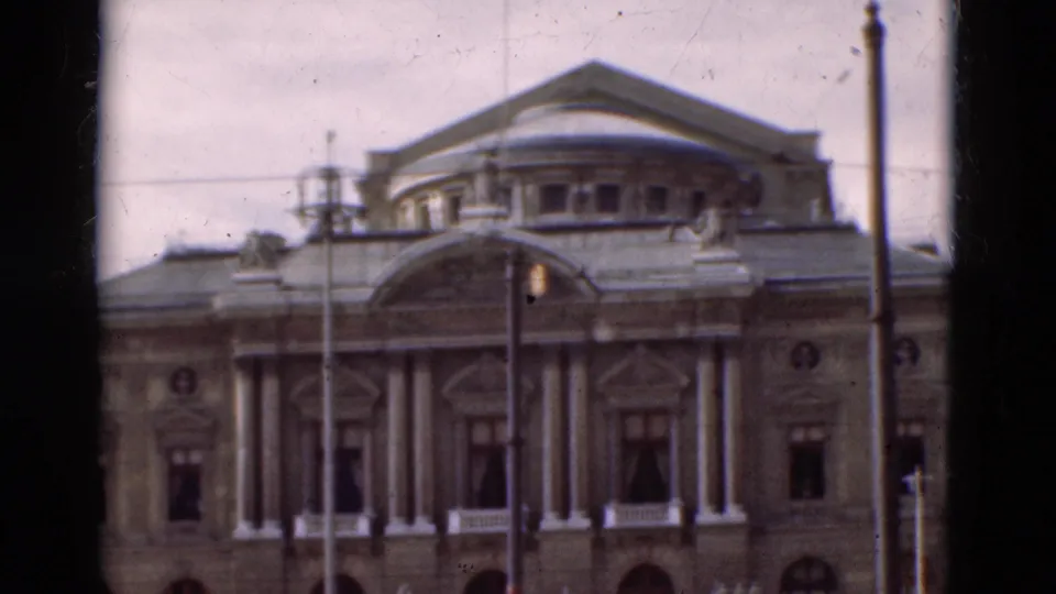 1975 Portugal 8mm frame showing a grand classical facade with columns, arched windows, roof detail, and street lamps in front.