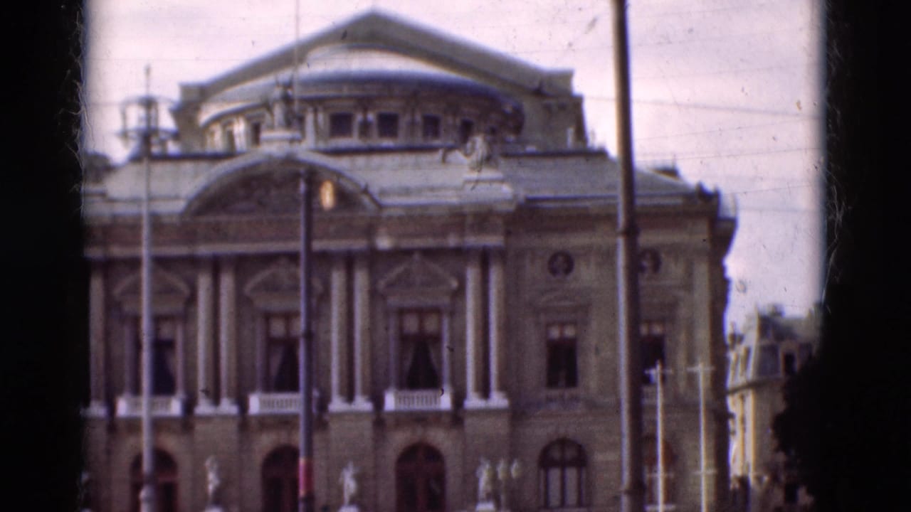Classical facade with columns, roof dome, street lamps, and a few distant pedestrians.