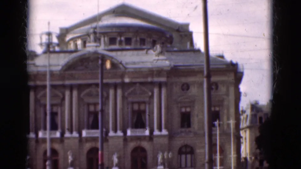 1975 Portugal travel footage frame showing an ornate urban building fronted by lamps, with distant people near the lower edge.