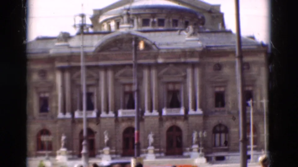 Soft 8mm view of a classical Portugal building in 1975, with vertical columns, arched windows, and street furniture in front.