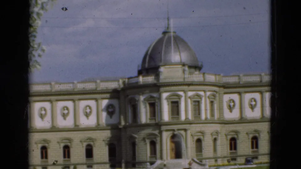 1975 Portugal 8mm frame of a large domed landmark building with decorative facade panels, arched windows, and a foreground lawn.