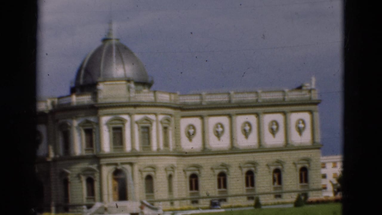 Classical pale building with a silver dome seen through dark window framing.