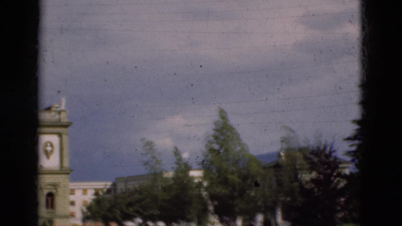 1975 Portugal 8mm frame showing a pale building partly obscured by trees, with dark window-like edges in the foreground.