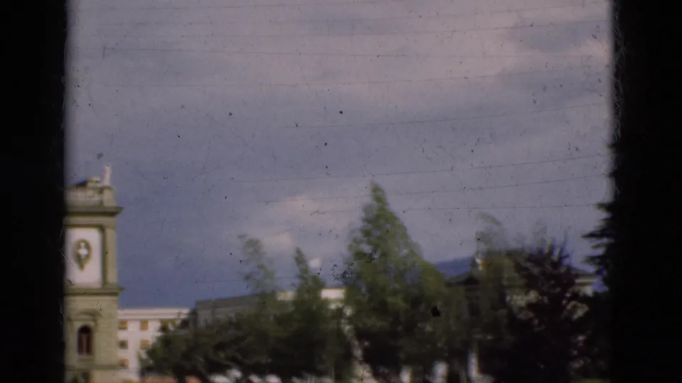 1975 Portugal 8mm frame showing a pale building partly obscured by trees, with dark window-like edges in the foreground.