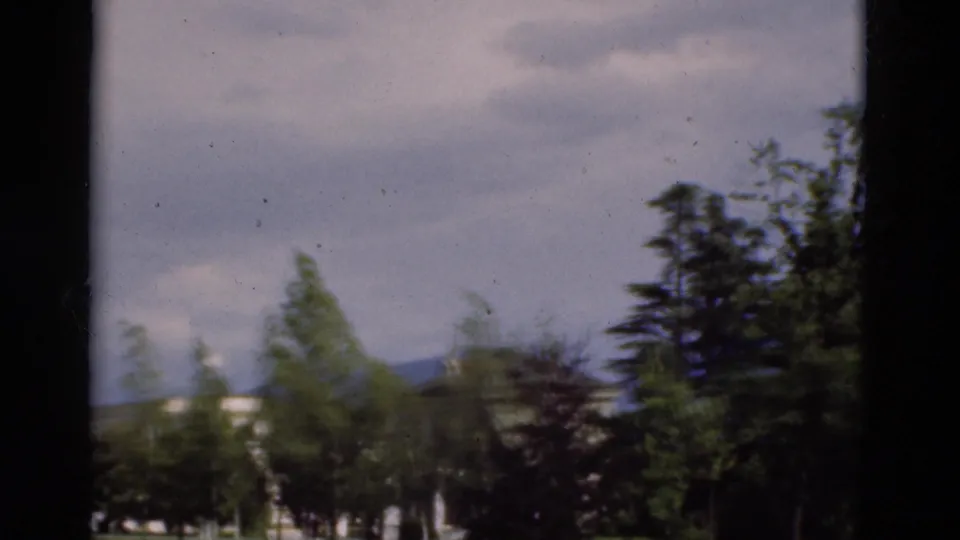 1975 Portugal 8mm view with trees, a pale building, distant hills, and a dark vertical foreground edge from the filming position.