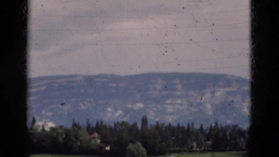 1975 Portugal 8mm frame showing a mountain ridge beyond a line of trees and grass, viewed through dark foreground framing.
