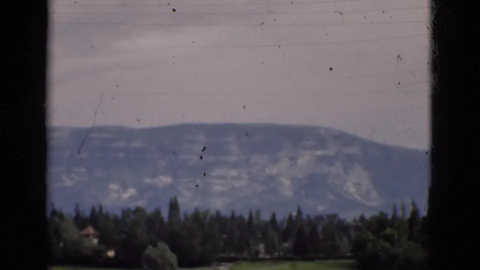 1975 Portugal 8mm view of a distant mountain ridge, dark tree line, and gray sky, still bordered by foreground frame edges.