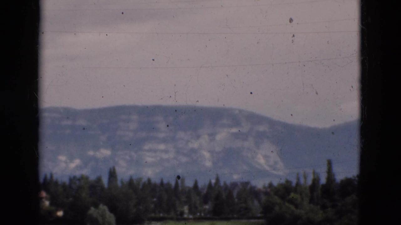 Distant mountain ridge beyond dark window framing and a line of green trees.