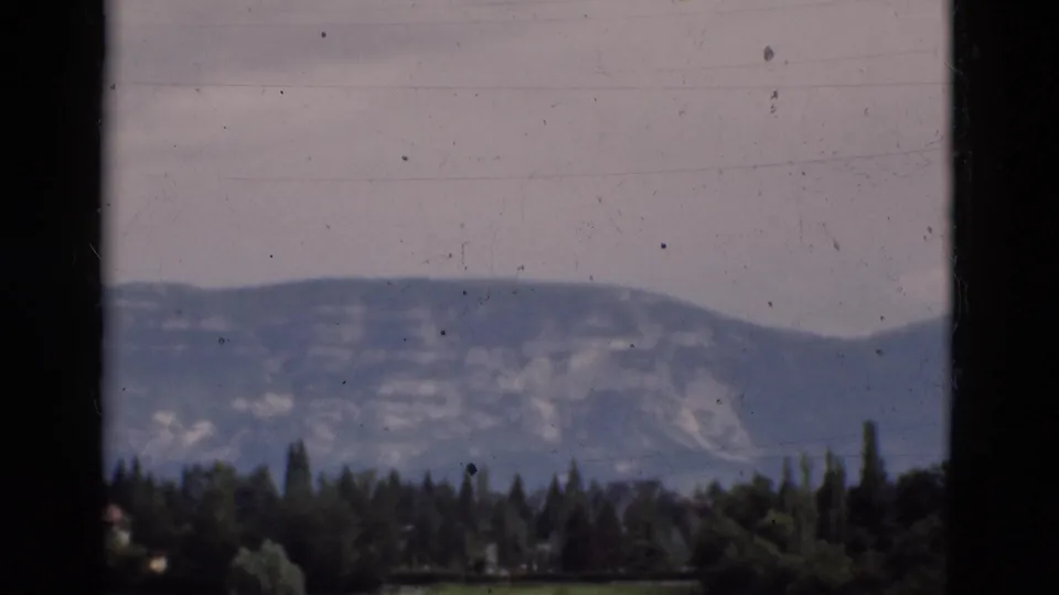 1975 Portugal 8mm view of a distant mountain ridge and green tree line seen through dark window-like framing.