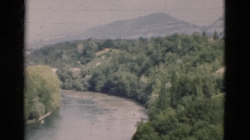 1975 Portugal 8mm view of a winding river cutting through green terrain, with hazy hills beyond.