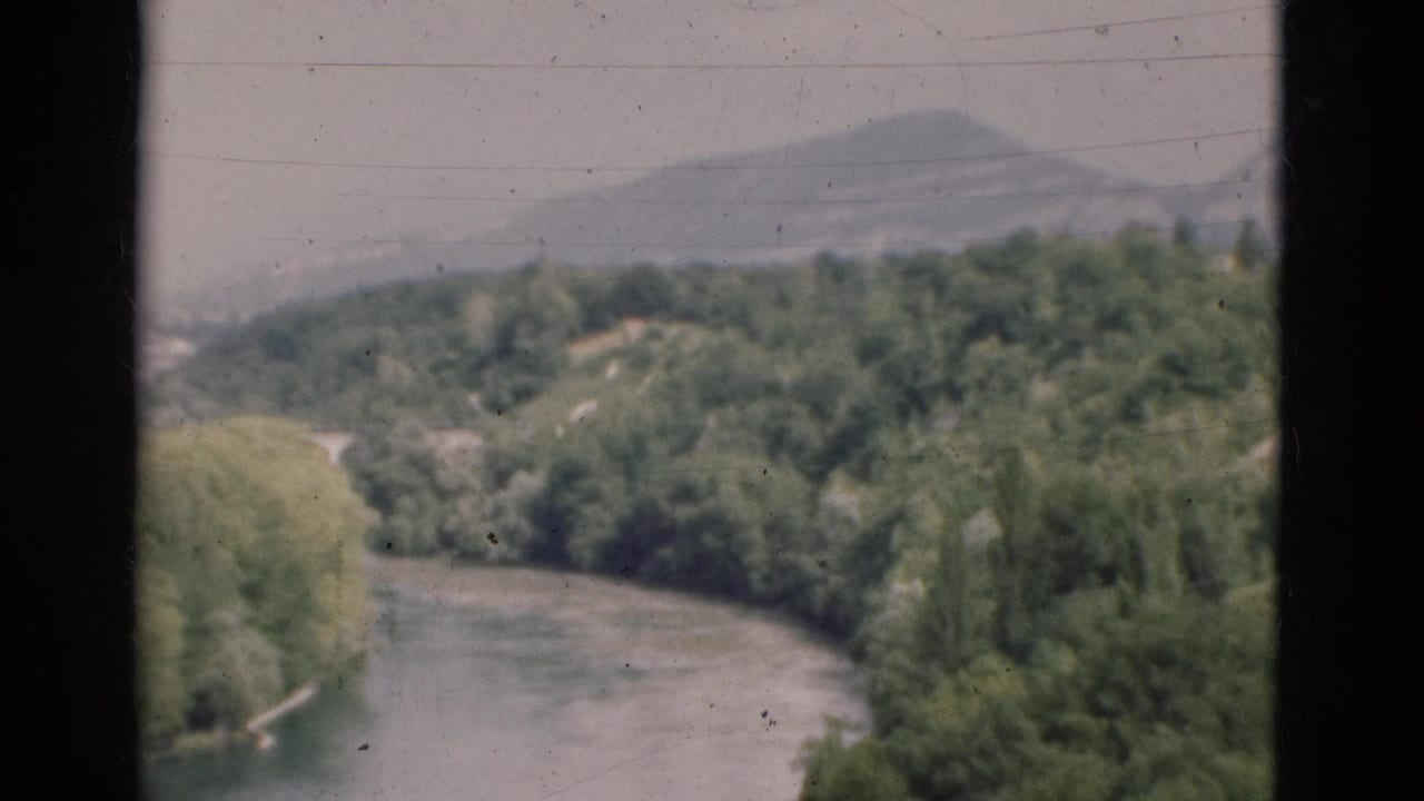River curves through green hills beneath a hazy sky, partly framed by dark window bars.
