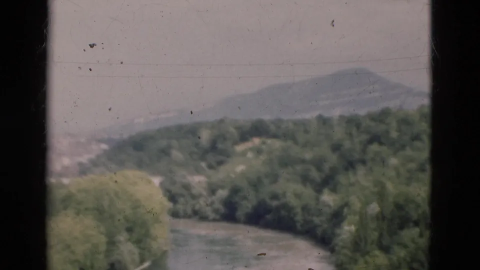 Window-framed 1975 Portugal travel view of a river, dense trees and hazy mountain slope.