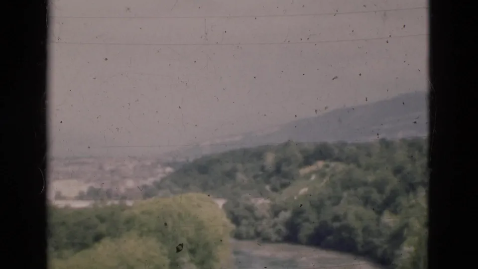 1975 Portugal 8mm landscape frame with river water, leafy banks, distant ridge and faded color.