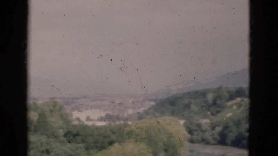 Portugal 1975 home-movie frame showing a hazy river valley, green hills and distant mountain forms.