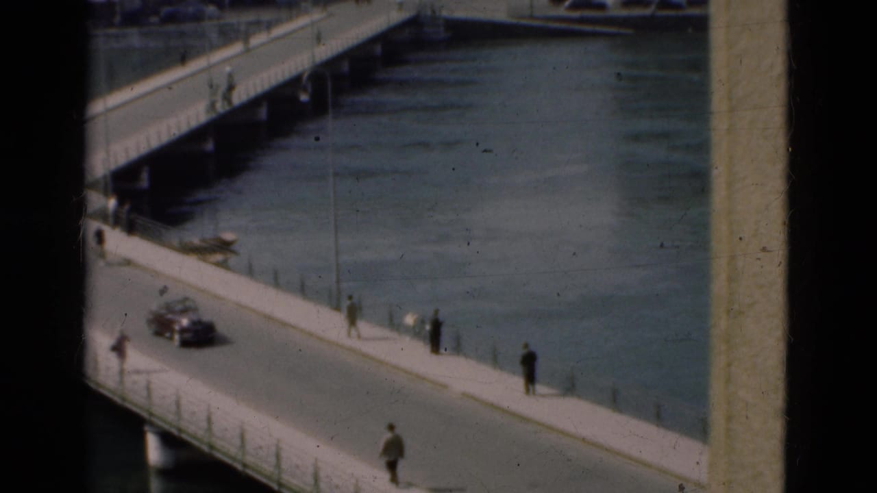 Bridge over a river with pedestrians on the sidewalk and a dark car on the road.
