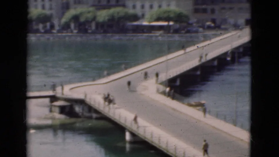 1975 Portugal home-movie frame showing a bridge approach and walkway over water with pedestrians in soft focus.