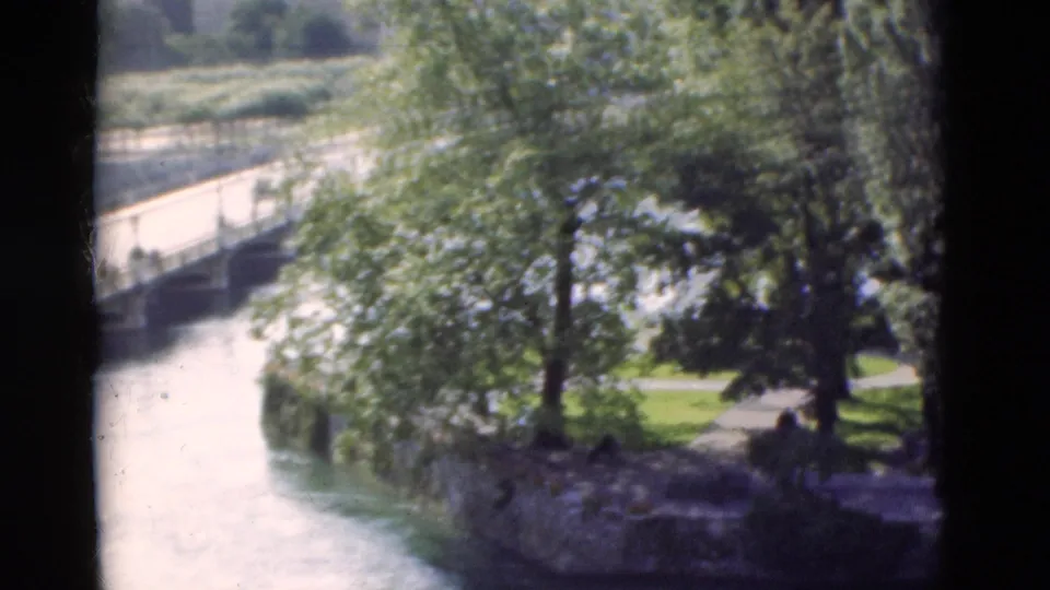 1975 Portugal home-movie view of bright river water, a stone riverside edge, trees, and green park lawn.