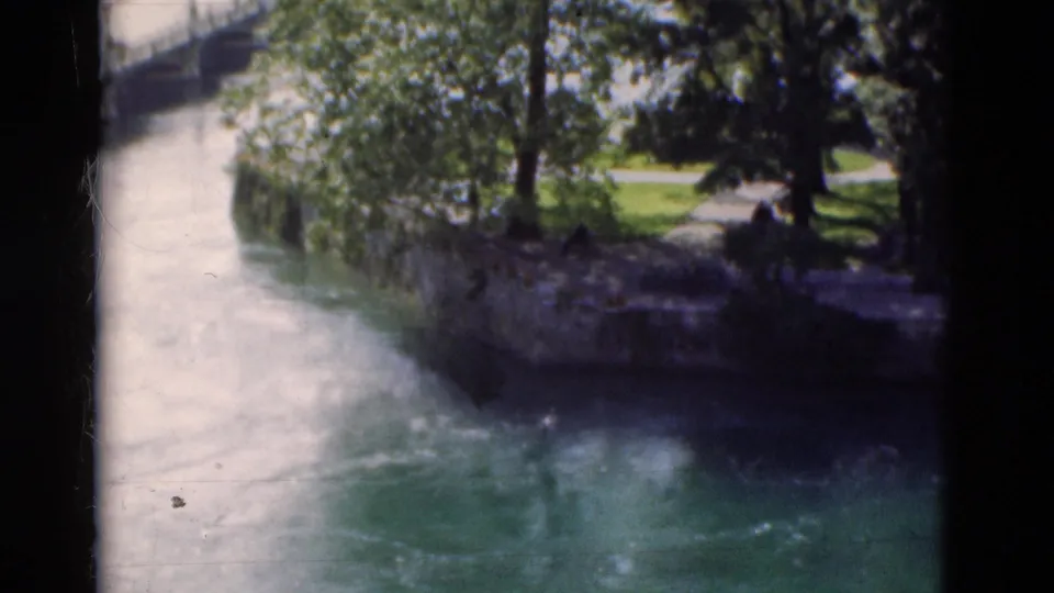 1975 Portugal 8mm frame looking over a river bend toward a tree-lined park with small distant people.