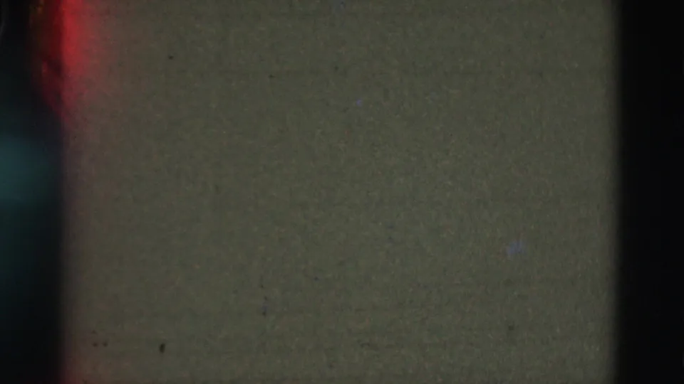 Dark 1975 Portugal 8mm frame showing muted green tone, heavy edge shadow, and a small reddish flare near the frame edge.