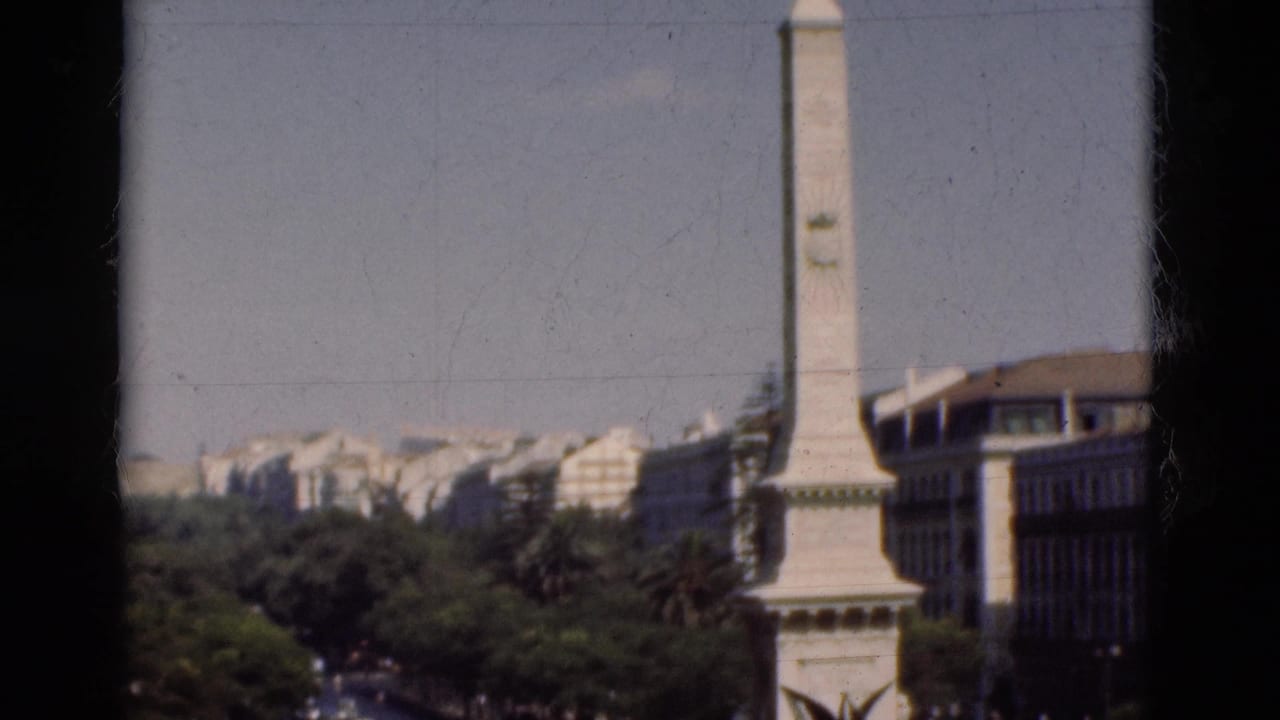 White obelisk monument rising above trees and city buildings under a pale sky.