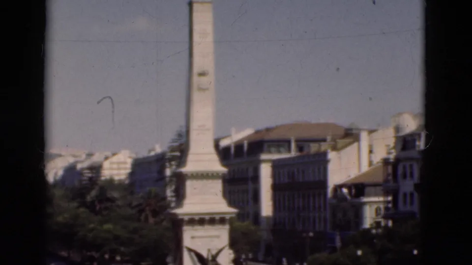 Final 1975 Portugal frame with the white monument, tree-lined foreground, surrounding buildings, and visible 8mm scratches.