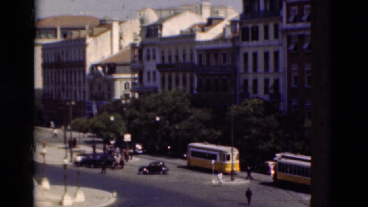 City roundabout with yellow trams, cars, pedestrians, trees, and multi-story buildings.