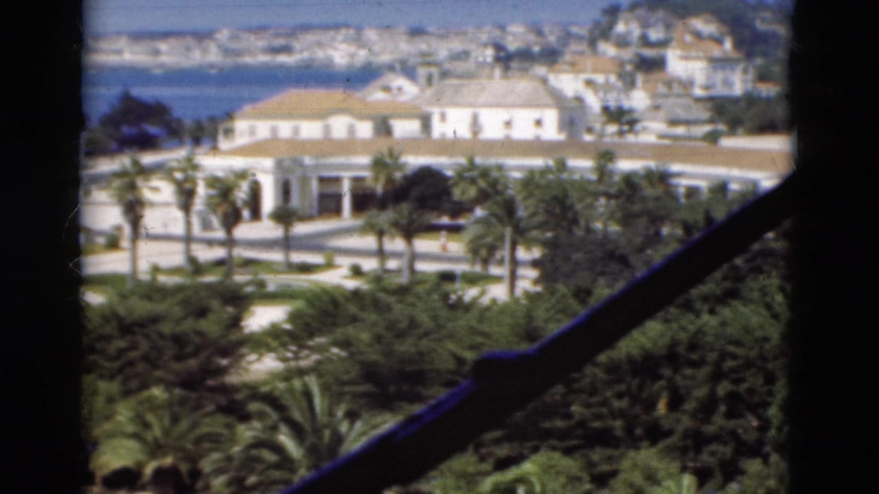 1975 Portugal home-movie view of white coastal buildings, palms, greenery, and sea seen through a window frame.